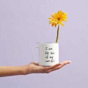 Hand holding a mug with a sunflower and motivational quote, set against a purple background.