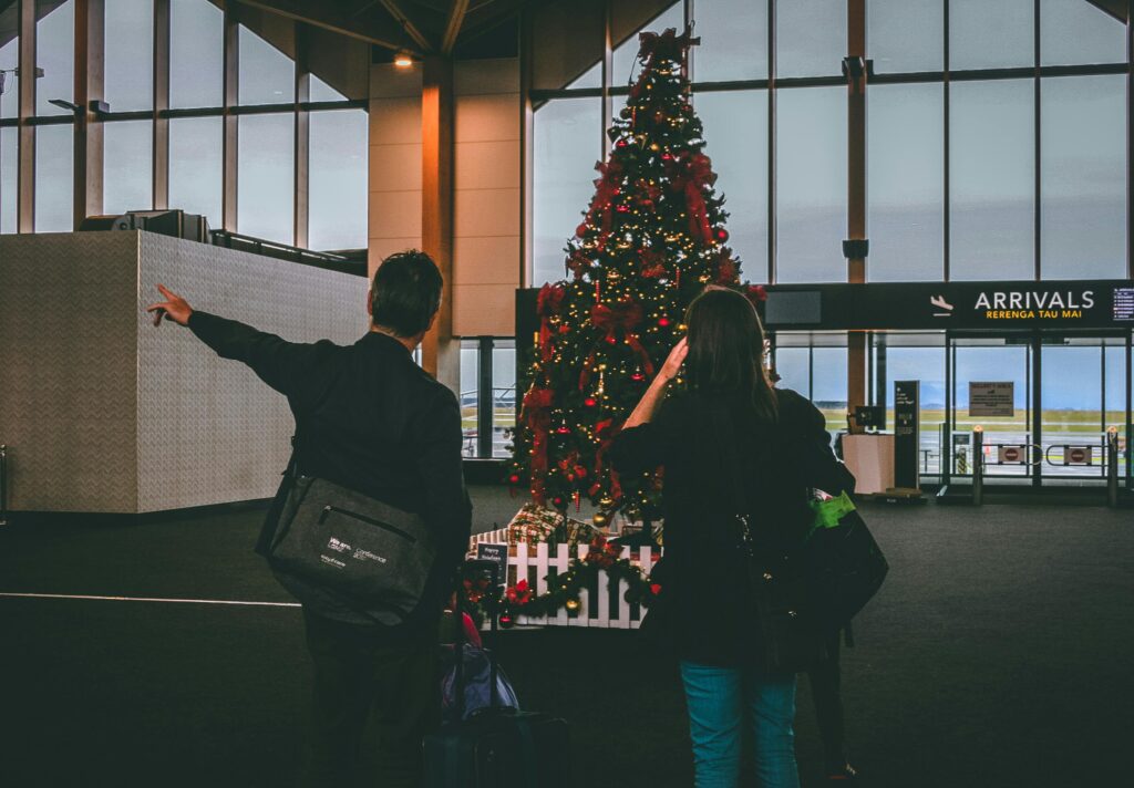 Couple at airport arrivals beside Christmas tree, holiday travel.