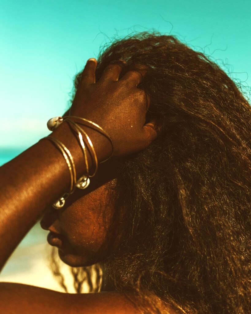 Editorial portrait of a woman touching her hair outdoors against a teal sky for the Mane Reads card