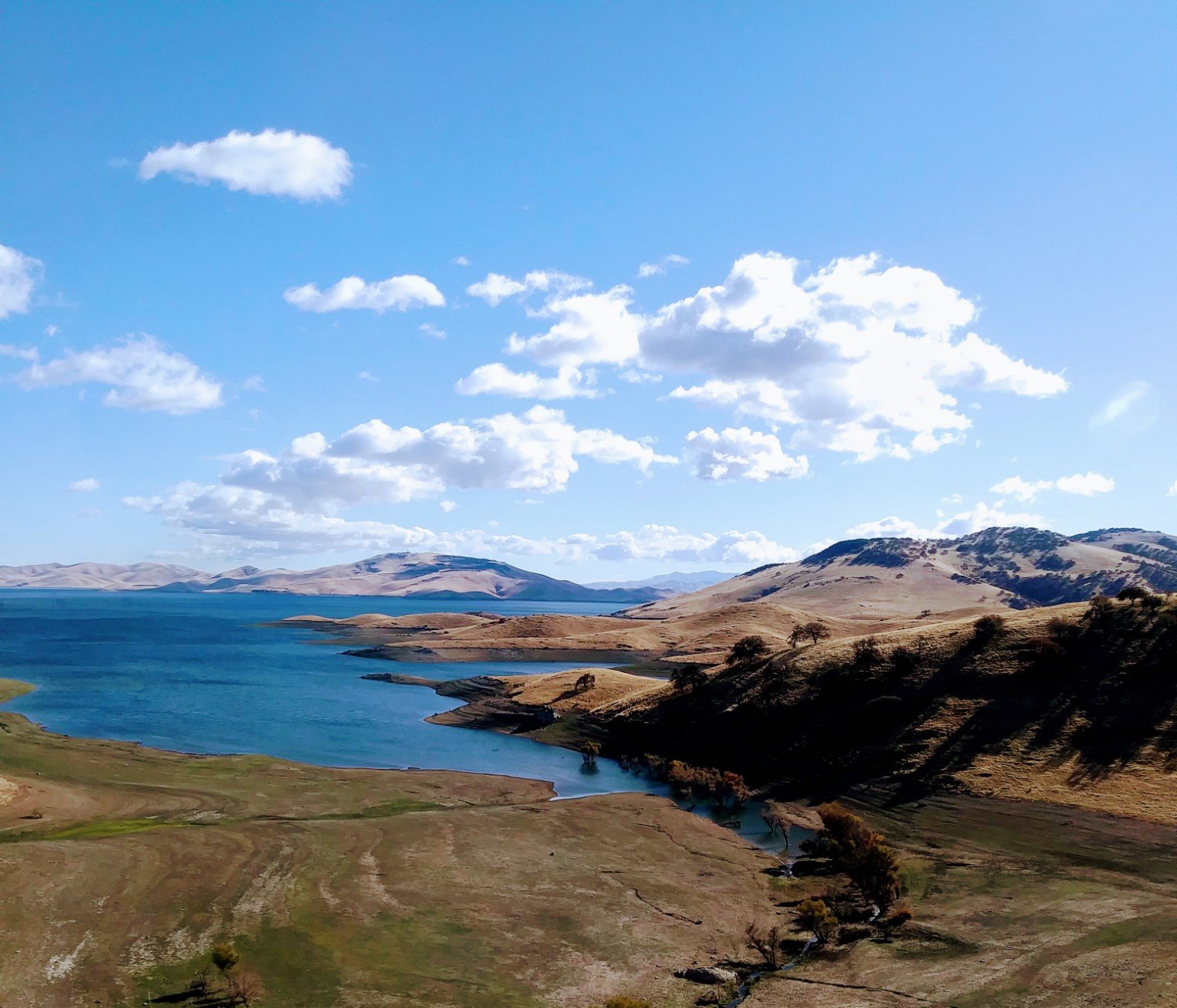 Scenic view of San Luis Reservoir surrounded by rolling golden hills in California
