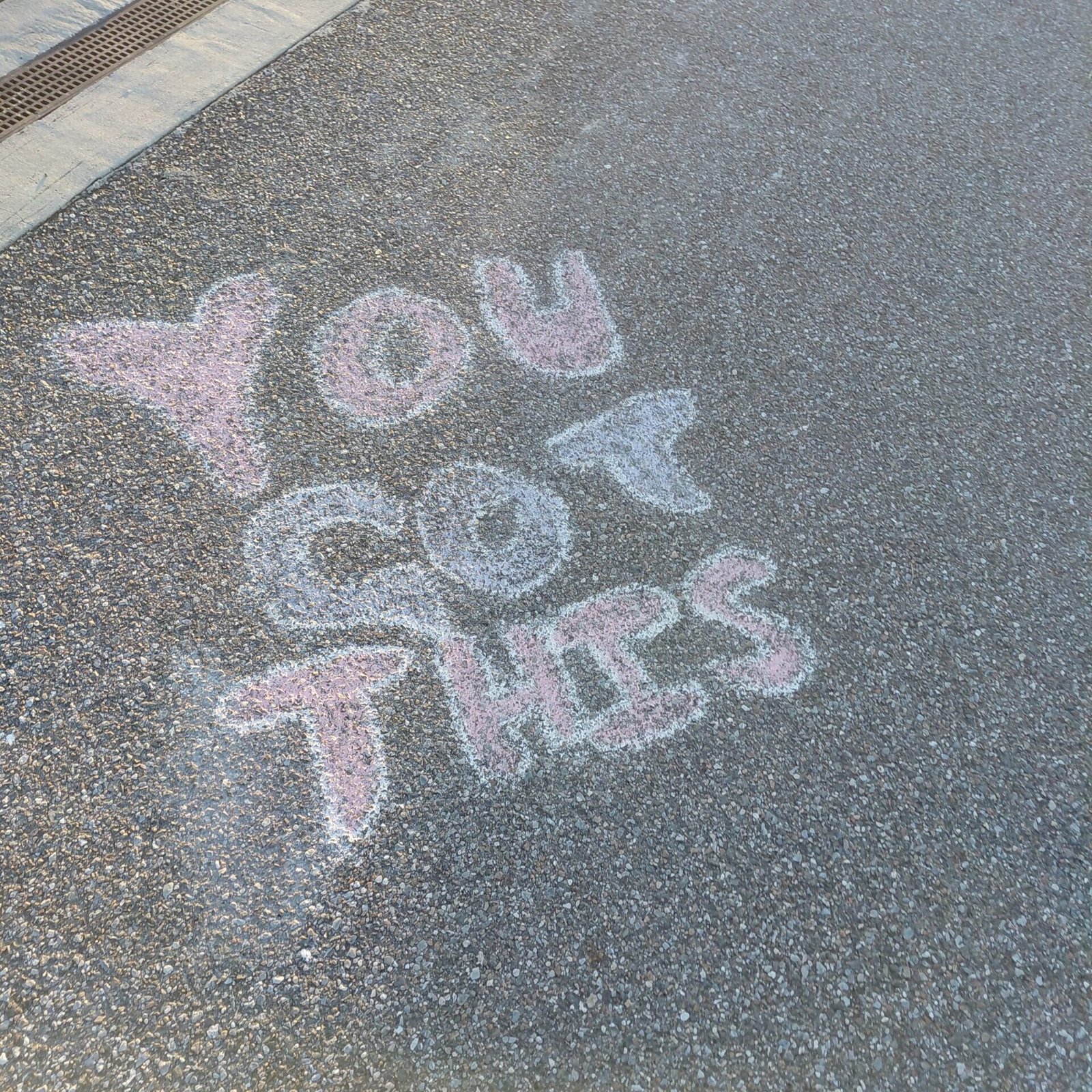 Colorful sidewalk chalk spelling YOU GOT THIS along a lakeside walking path