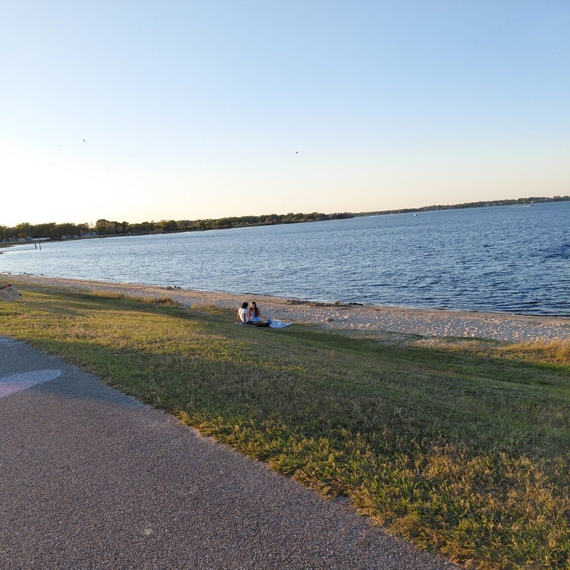 Two people sitting together beside a peaceful lake on a sunny afternoon