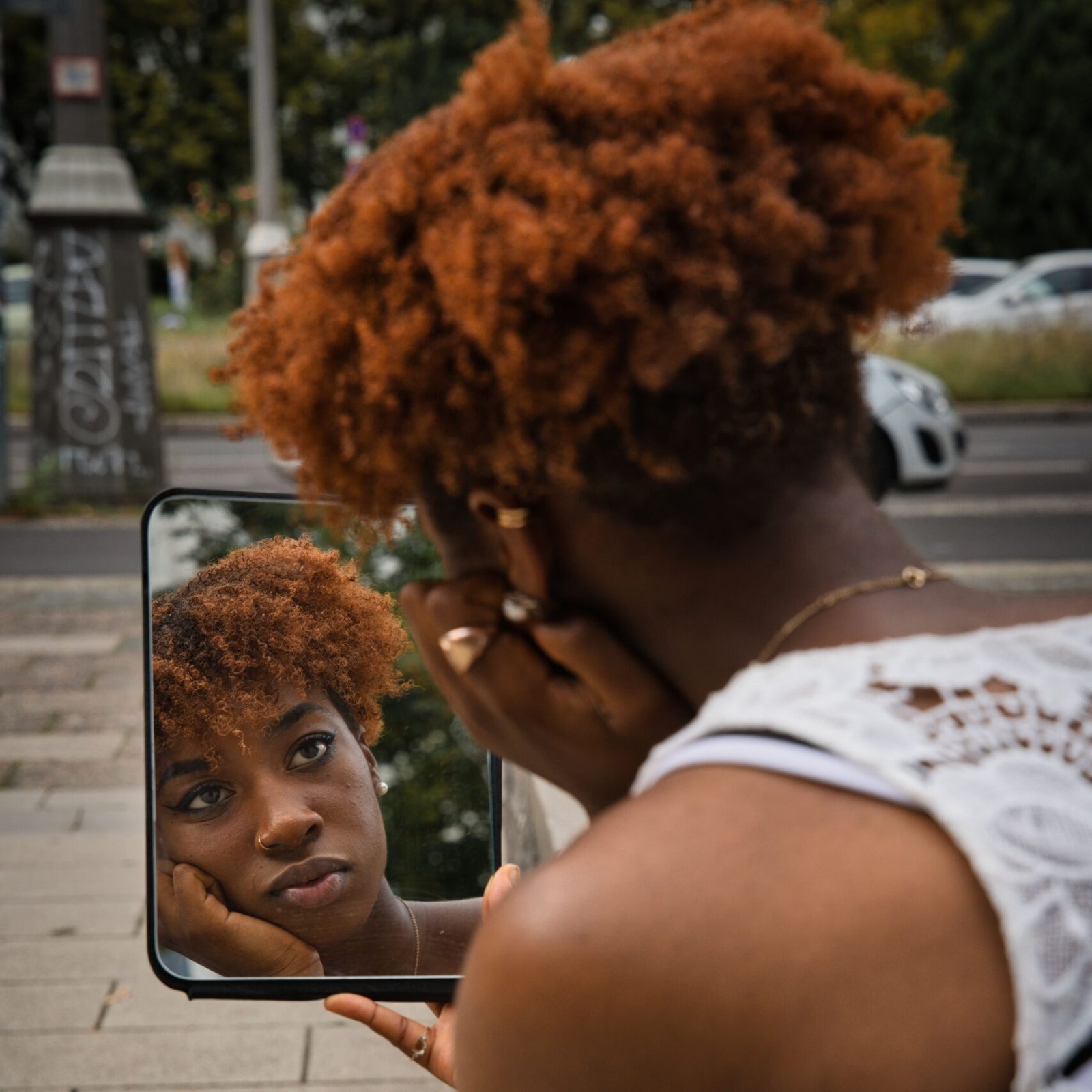 Woman with natural hair looking at her reflection in a handheld mirror outdoors